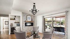 A modern living room with a fireplace, a chandelier, and a view through large sliding doors. - Resort-Style Escape: Pool, Courts, and Endless Fun (Scottsdale)