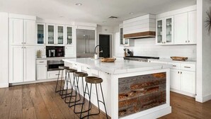 A modern kitchen with white cabinetry, a central island with stools, and a rustic wood accent. - Resort-Style Escape: Pool, Courts, and Endless Fun (Scottsdale)