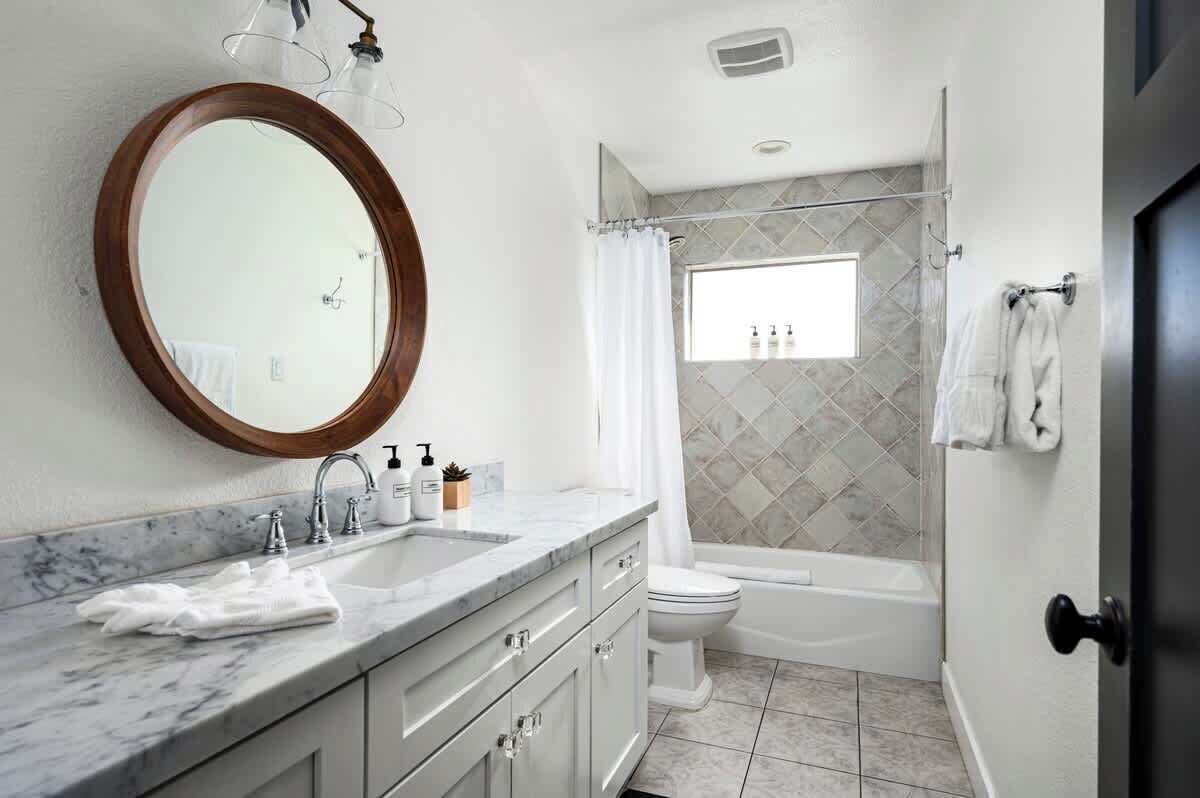 A bathroom with a marble sink, a wooden-framed mirror, a shower curtain, a toilet, and a bathtub.