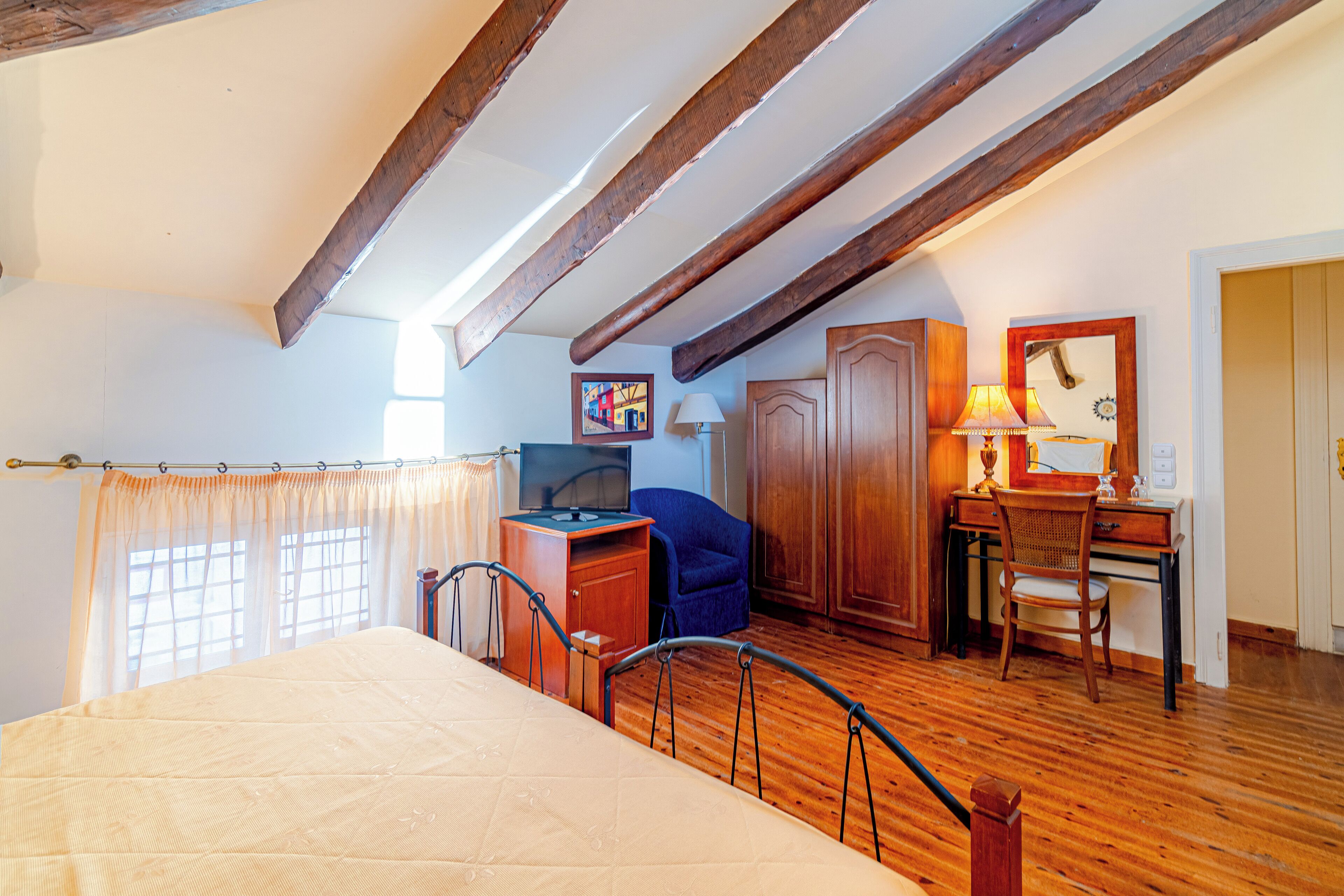 A bedroom with a bed, wooden desk, chair, television, and a cabinet.