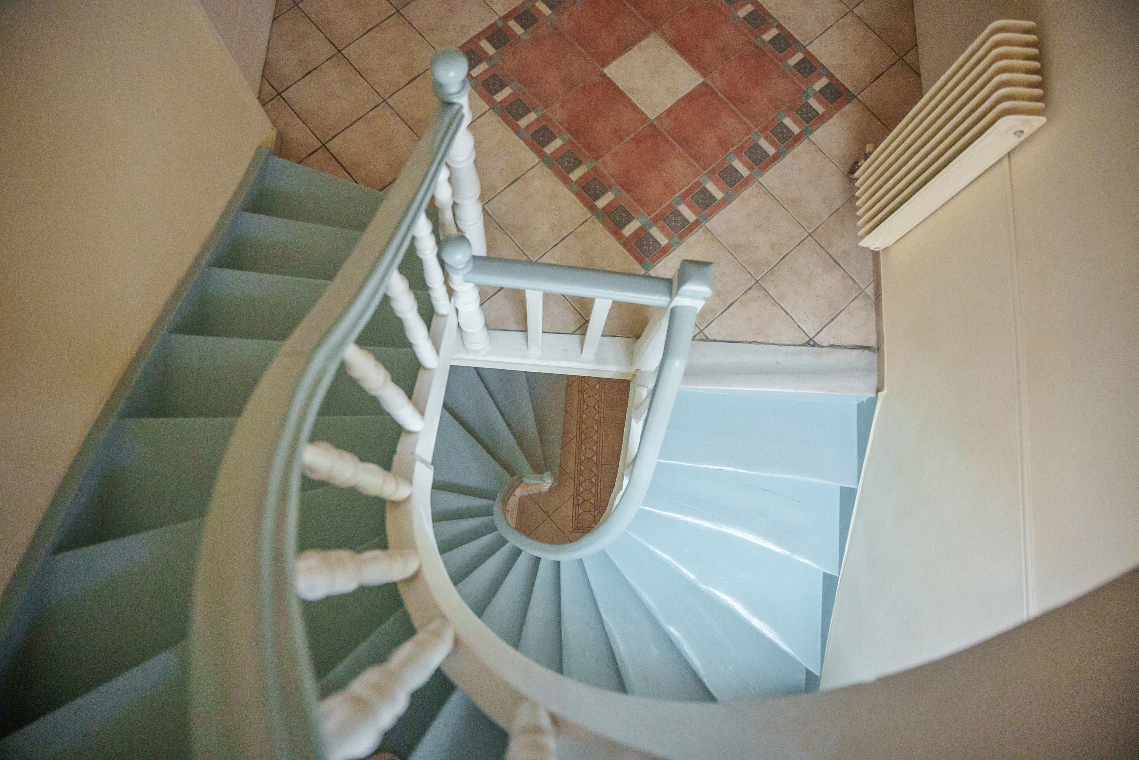 A spiral staircase with white balusters and a wooden handrail, leading to a landing with a patterned floor.