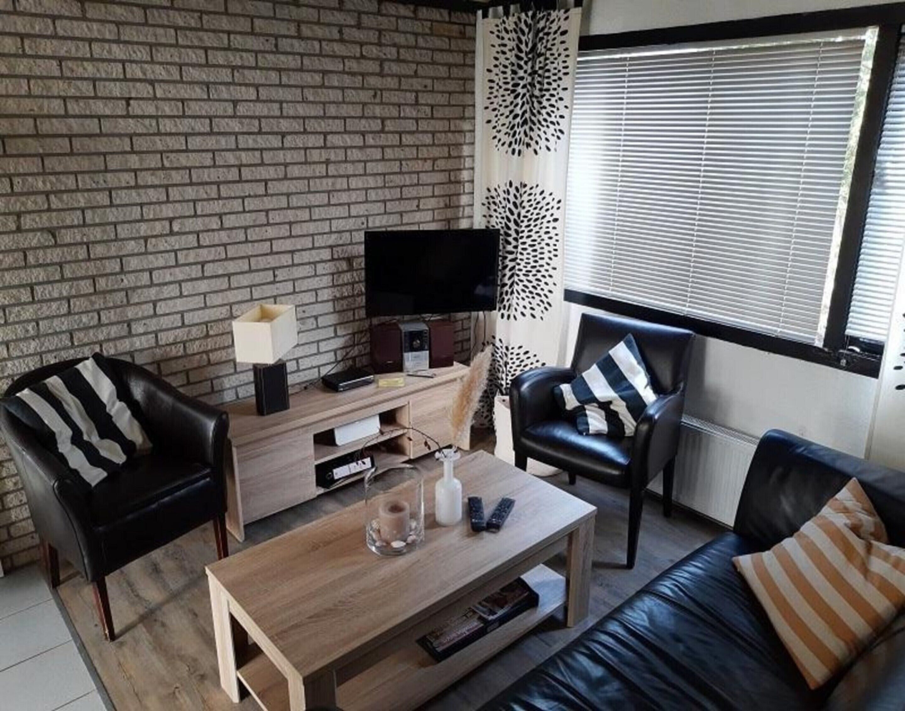 A modern living room with a brick wall, a flat-screen TV, a wooden coffee table, and two leather sofas with striped pillows.
