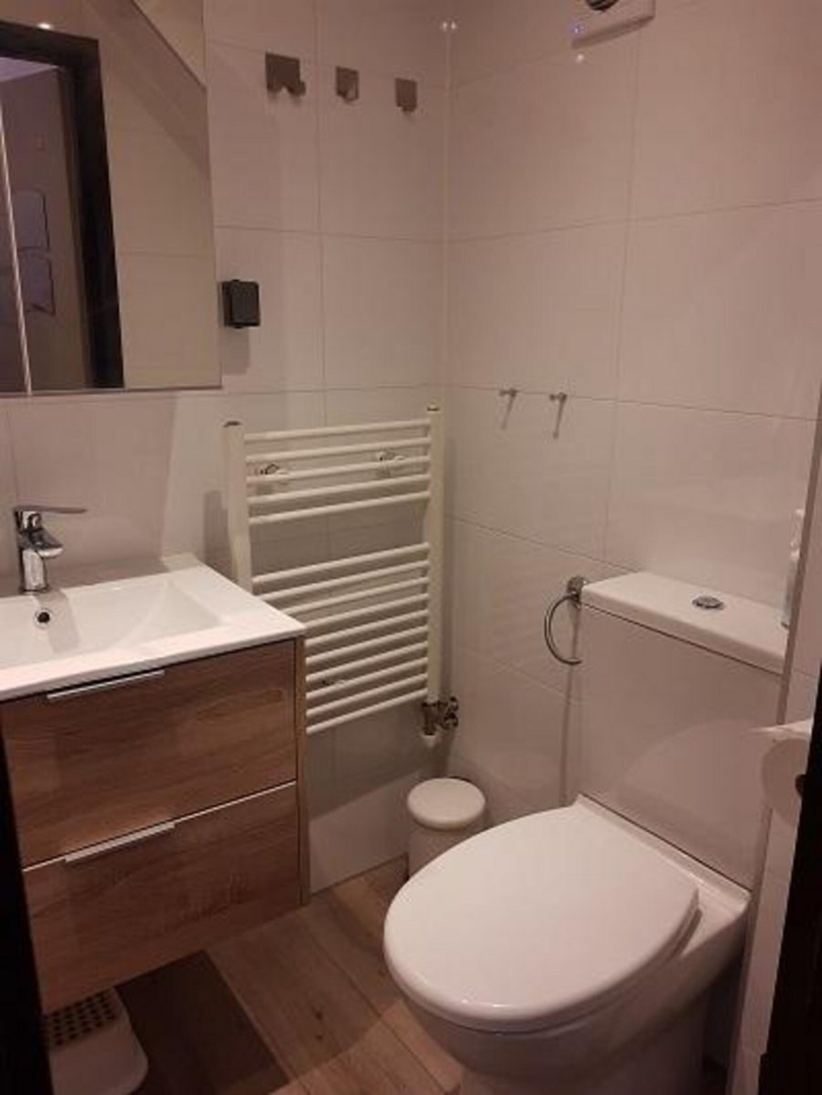 A modern bathroom with a white sink, wooden cabinet, toilet, and a towel rack.