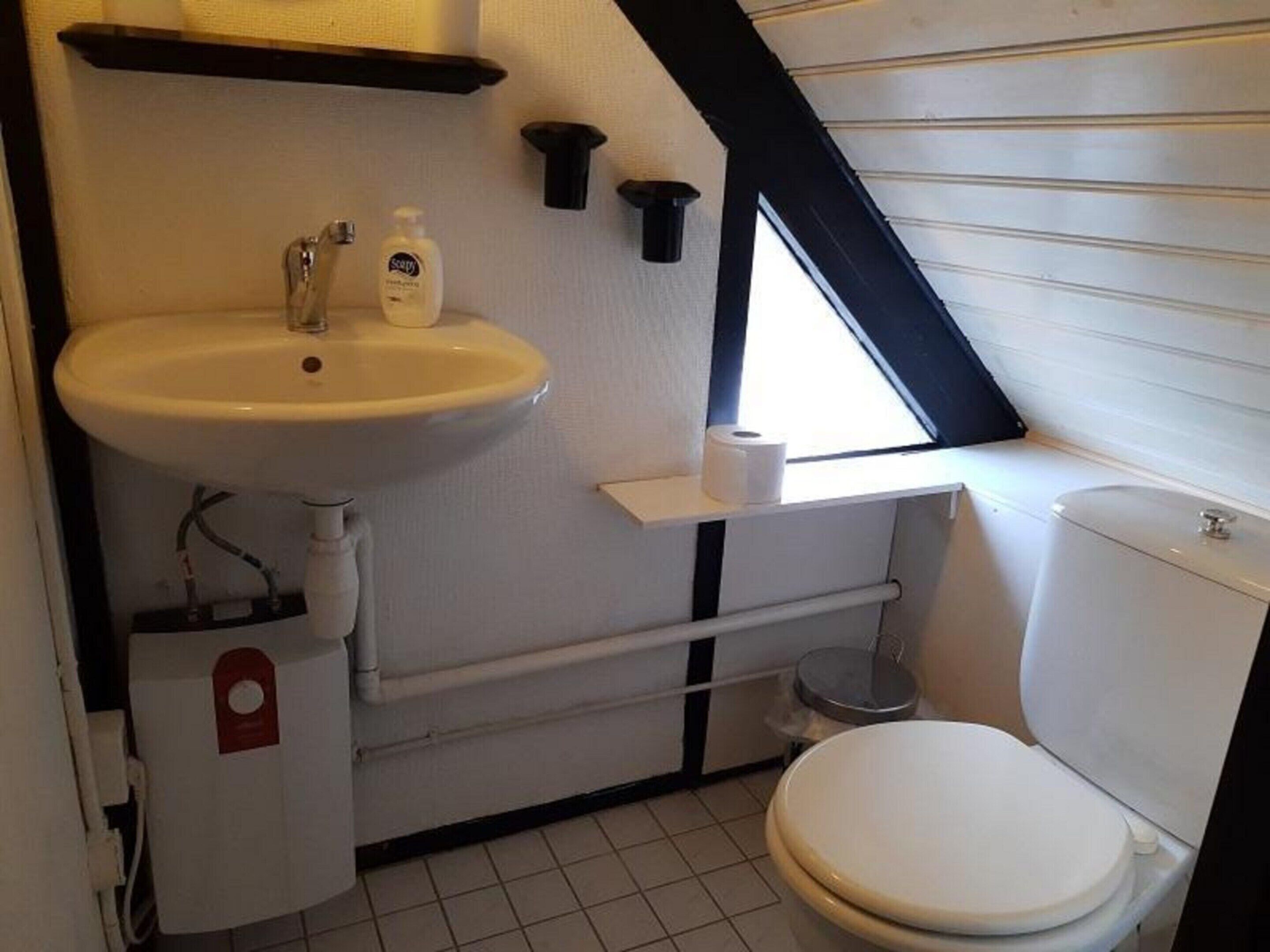 A small, compact bathroom with a white sink, toilet, and a window providing natural light.