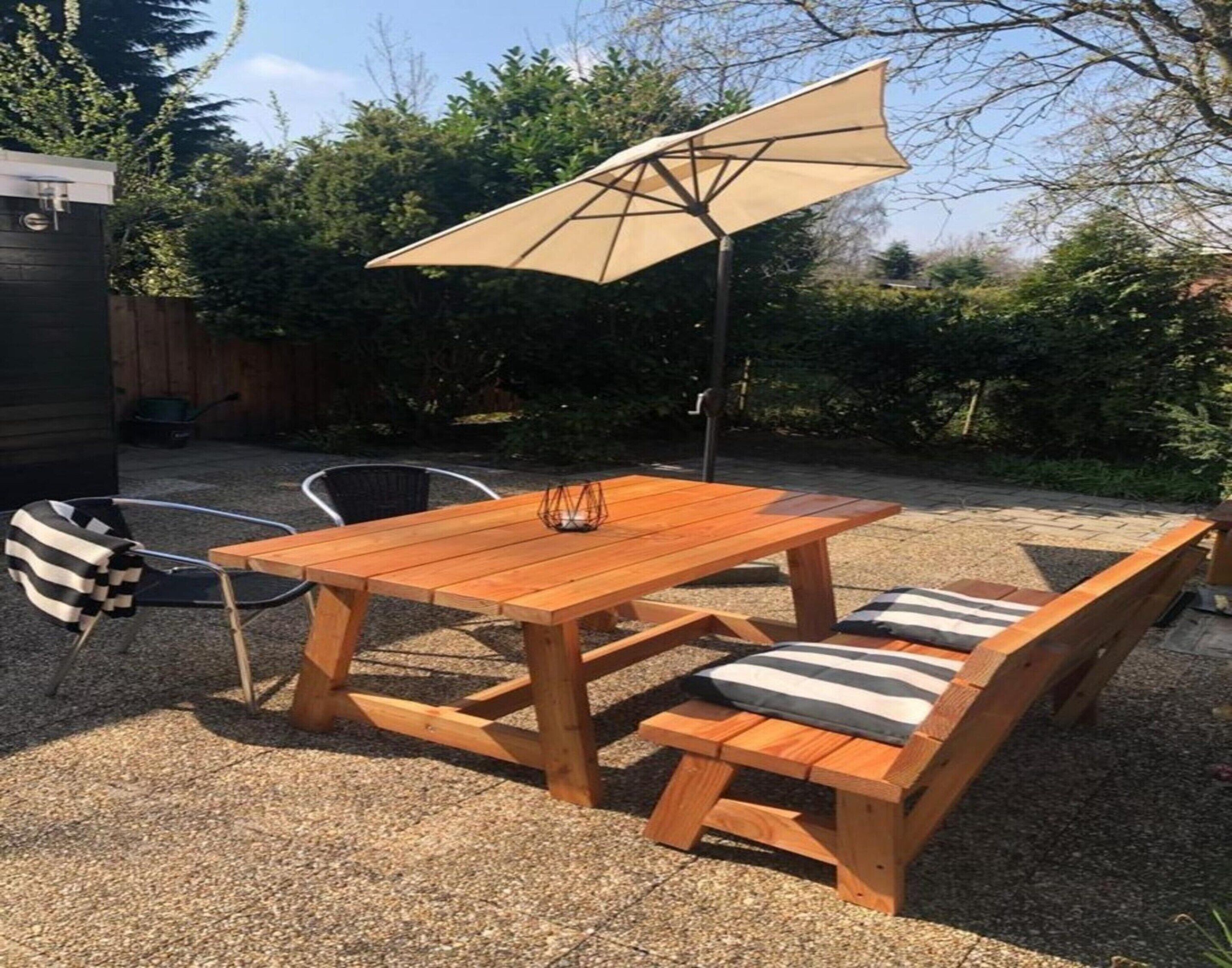A wooden patio table with benches, an umbrella, and a chair.