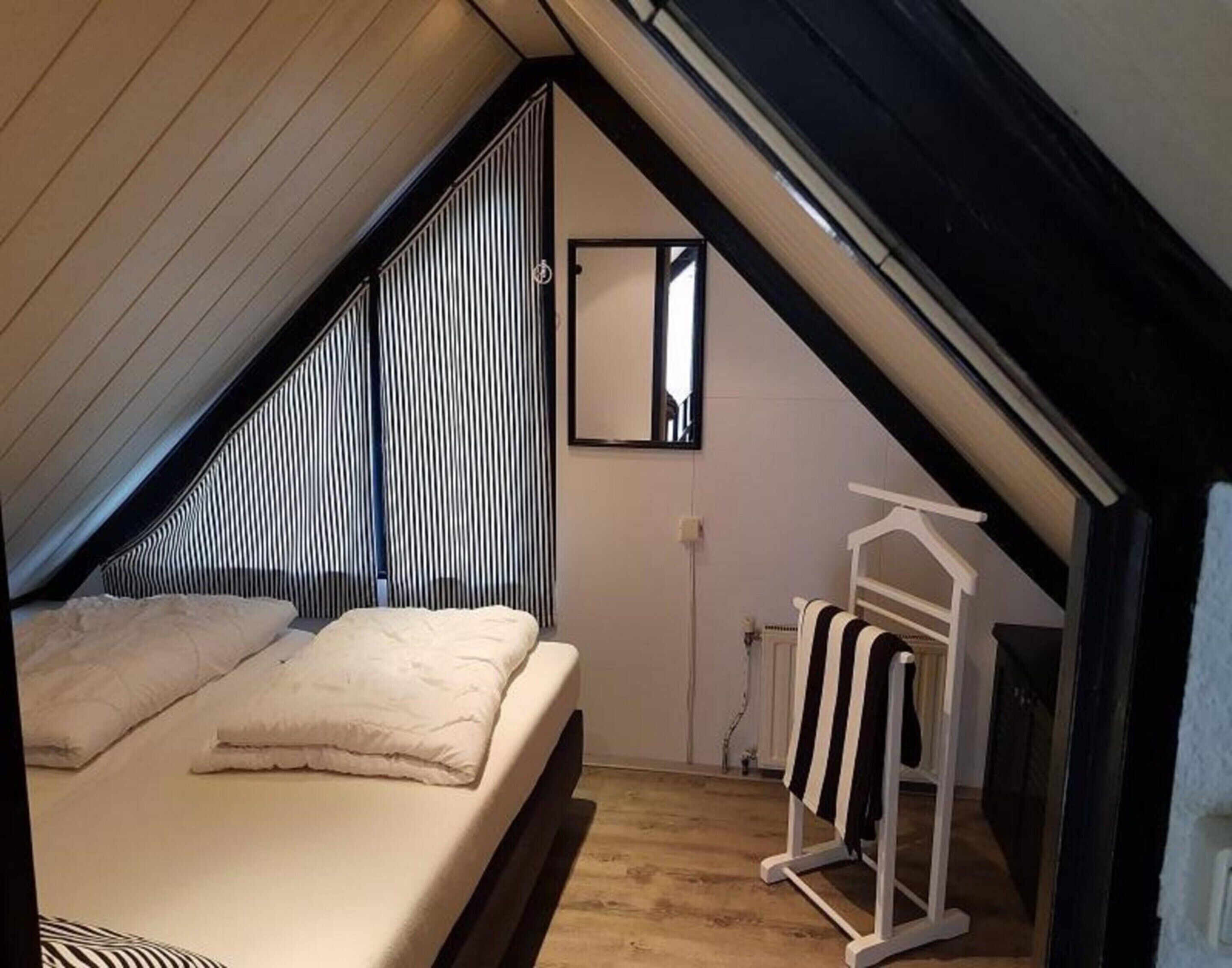 Ein Schlafzimmer mit schrägverdeckter Decke, einem Bett mit weißer Bettwäsche, einem Heizkörper und einem weißen Kleiderständer.