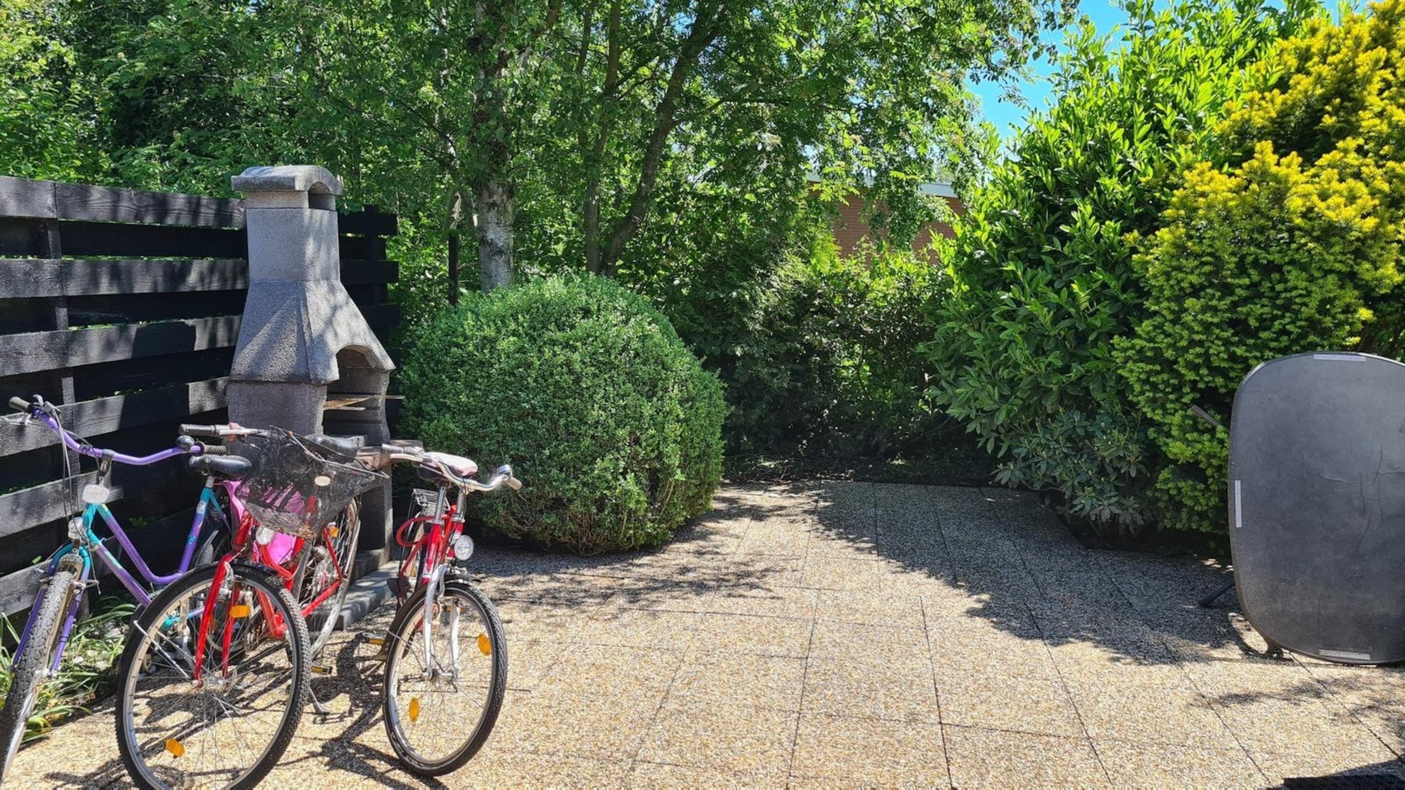 A paved pathway with bicycles parked on the left, surrounded by lush greenery and a wooden fence.