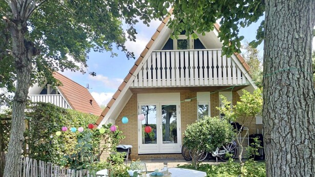 Une maison avec un toit en pente, un balcon et un jardin clos, aménagé avec une table et des chaises.