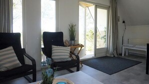 Une pièce avec deux chaises noires, une petite table sur laquelle se trouve une plante, un banc et une vue dégagée sur l’extérieur grâce à de grandes fenêtres.