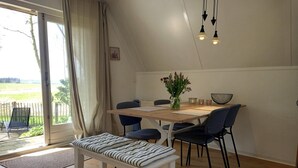 Un coin repas avec une table en bois, des chaises, un banc, un vase de fleurs et une vue à travers une porte vitrée.
