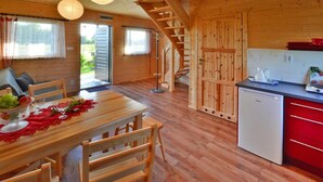 Interno di una baita in legno con tavolo da pranzo, sedie, una scala e angolo cottura.