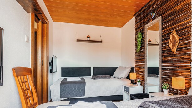Una camera da letto moderna con soffitto in legno, un letto con copripiumino grigio e bianco, un comodino con una lampada e uno specchio a parete.