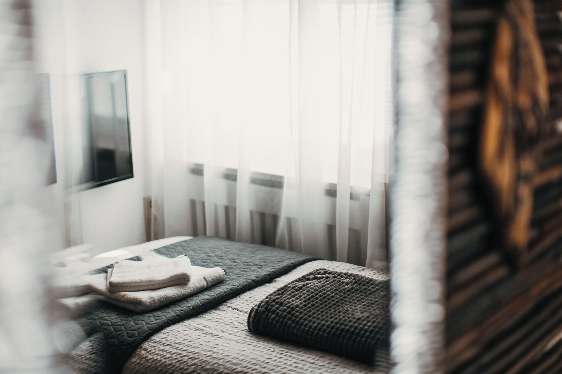 Ein Schlafzimmer mit Bett, Nachttisch und Fenster mit transparenten Vorhängen.
