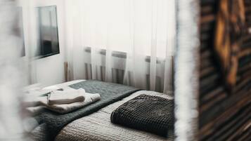 Ein Schlafzimmer mit Bett, Nachttisch und Fenster mit transparenten Vorhängen.