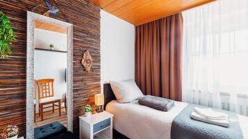 A modern bedroom with a wooden ceiling, a bed with a grey quilt, a nightstand with a lamp, a chair, and a mirror with a decorative frame.