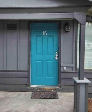 Welcome to a charming entrance with a teal door, decorative welcome mat, and a simple lantern above.