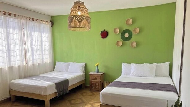 A room with two single beds, a hanging lamp, a small table with a vase, and a wall decoration. - Hostal Alixel Oaxaca (Oaxaca)