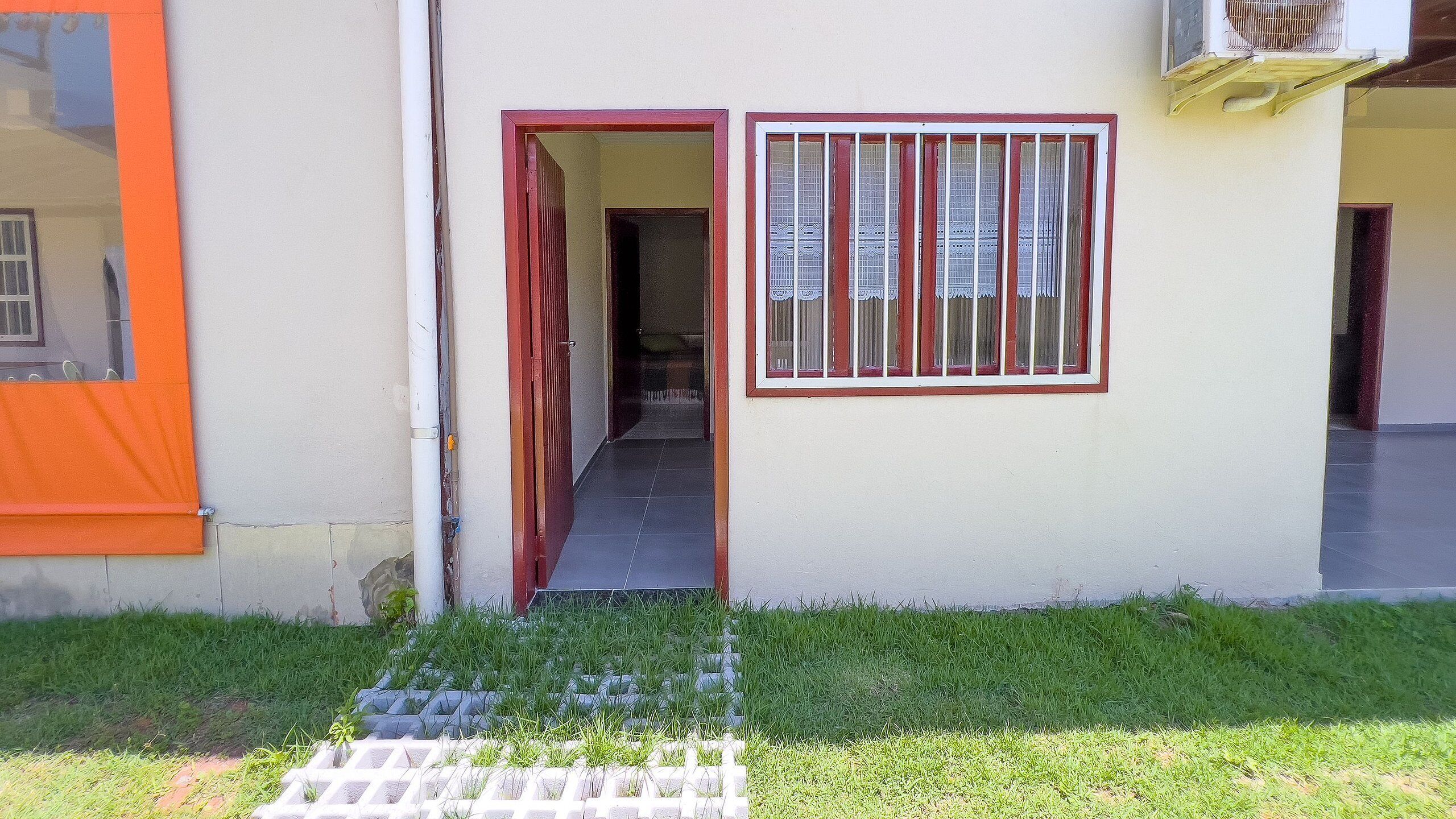 A building entrance with a red door, a barred window, and a small garden area.