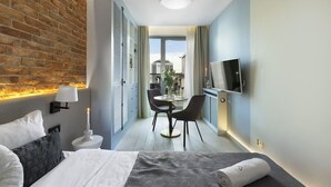 Ett modernt hotellrum med en accentvägg i tegel, en säng med vita sängkläder, ett sängbord med en lampa, ett litet runt bord med stolar och en tv som är monterad på väggen.