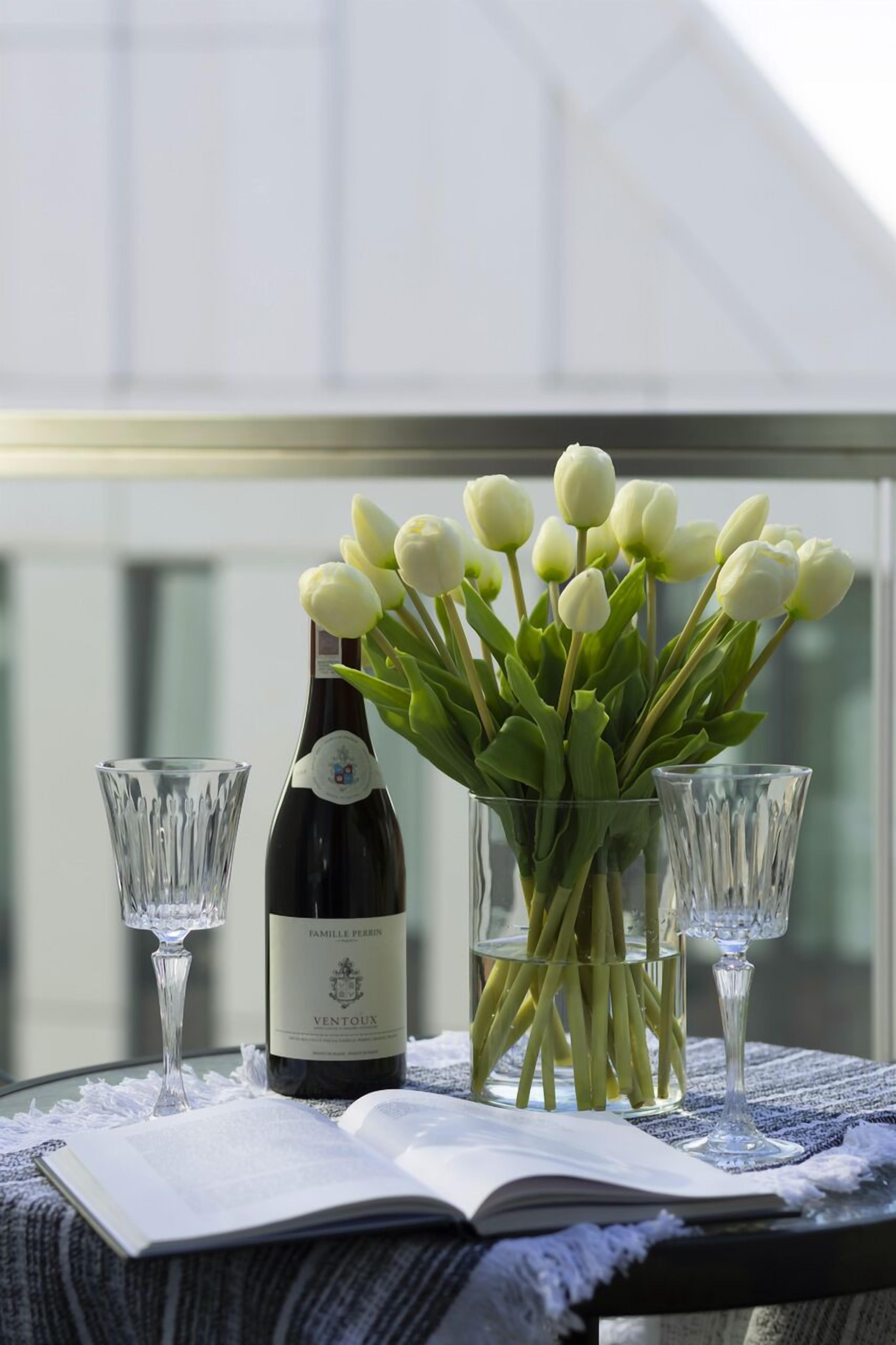 Une table avec une bouteille de vin, un vase de tulipes et deux verres posés sur une nappe.