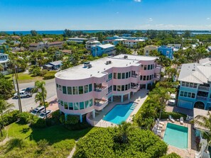 A multi-story building with a swimming pool, surrounded by greenery and a clear view of the ocean.