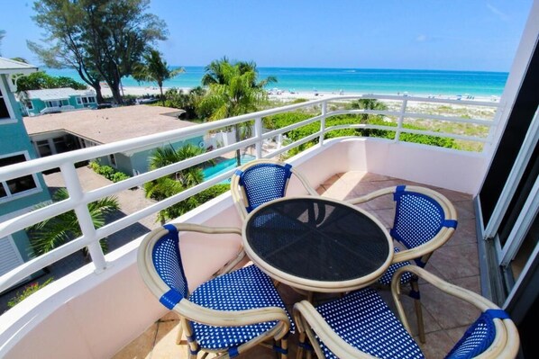 A balcony with a table and chairs, overlooking a beach and ocean.