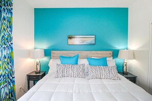 A neatly made bed with white bedding and blue pillows, a teal accent wall, and a framed picture above the bed.