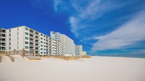 A beachfront hotel with multiple floors, balconies, and a sandy beach in the foreground.