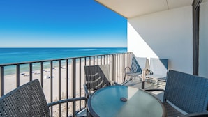 A balcony with a table and chairs, overlooking a beach with umbrellas.