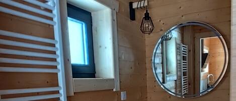A wooden cabin interior with a window, a mirror, and a sink.