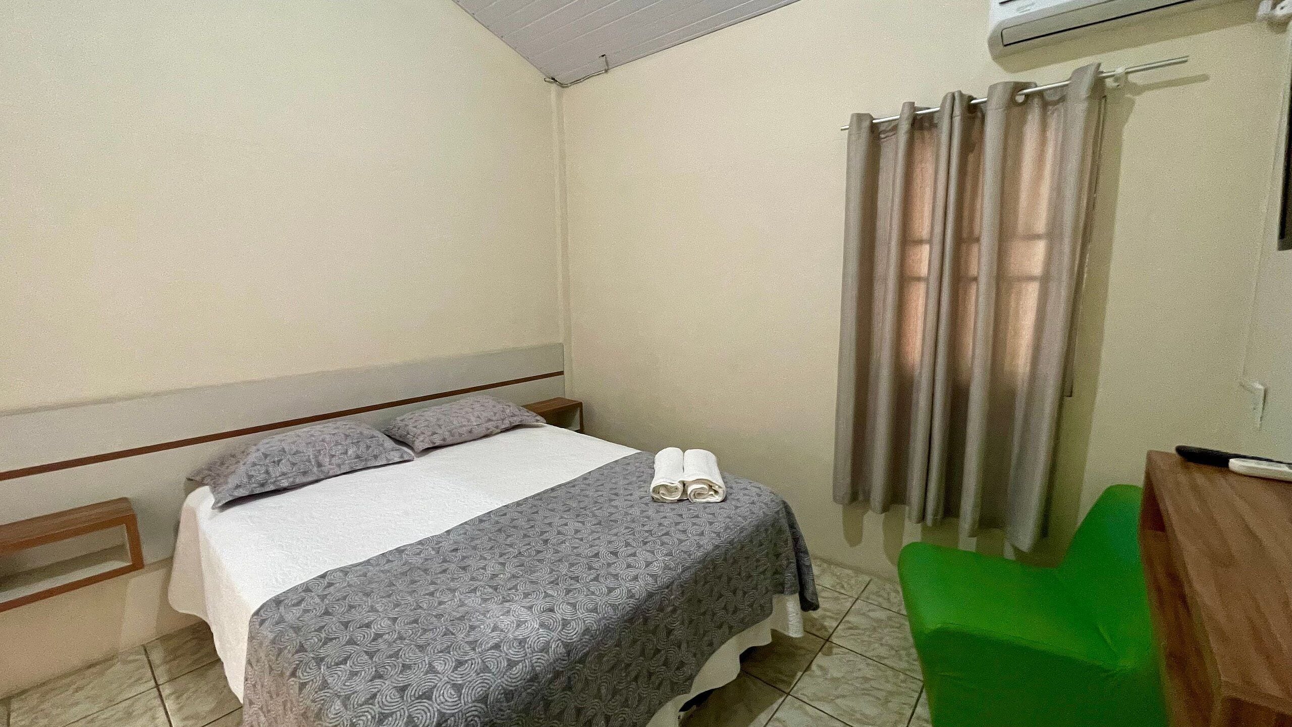A bedroom with a bed, pillows, a green chair, a desk, and a curtain.