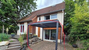 A house with a paved patio, a pergola, and a red garden hose.