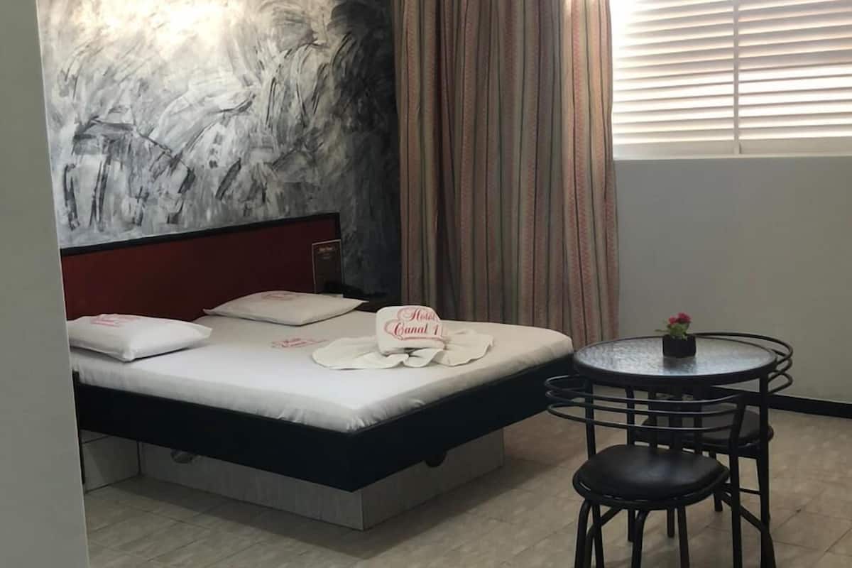 A hotel room with a bed, a ceiling fan, a round table with chairs, and a window with blinds.
