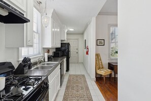 Une cuisine avec des meubles blancs, une cuisinière noire et un coin repas comprenant une chaise et une table.