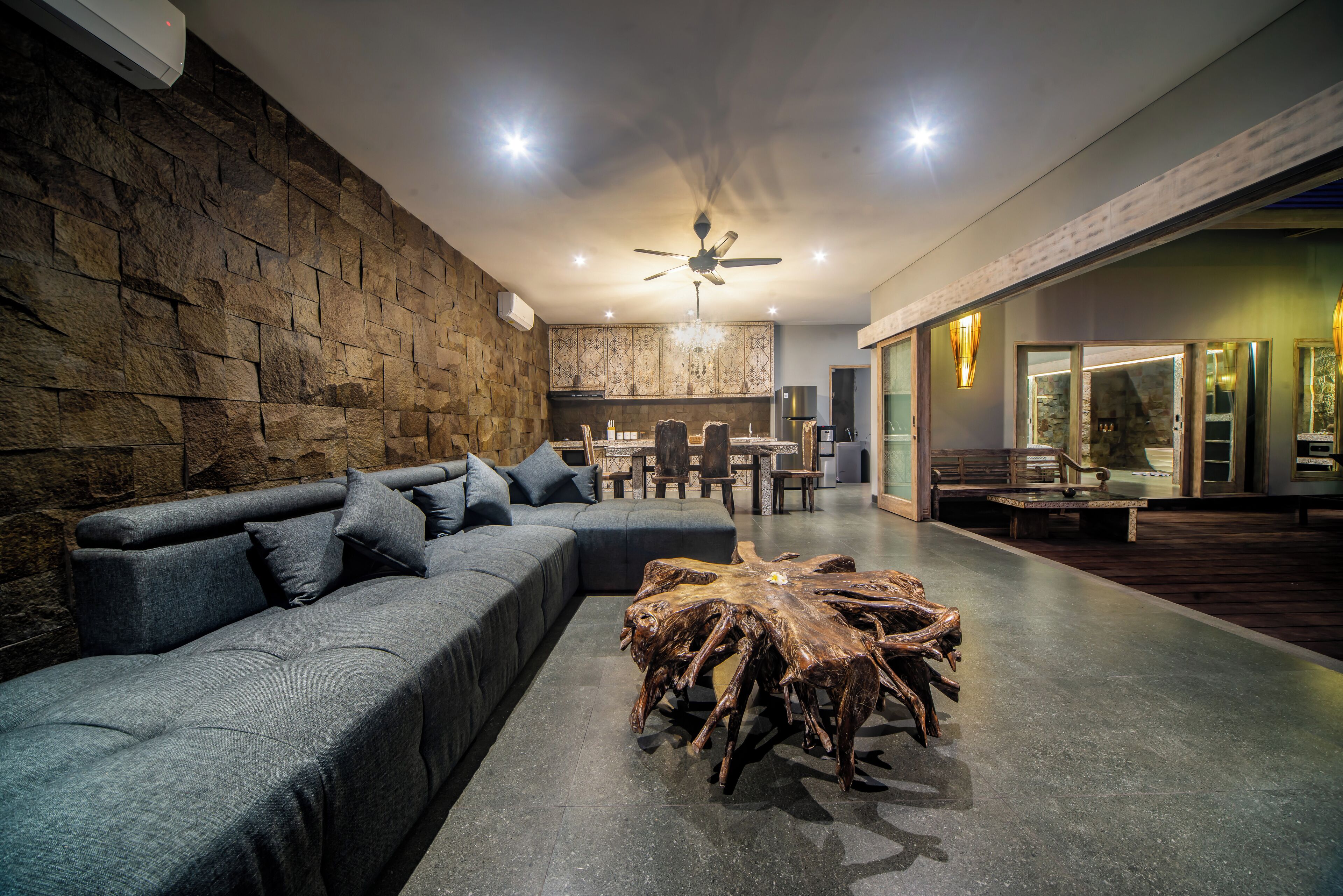 A modern living room with a stone wall, a grey sofa, a wooden coffee table, and a ceiling fan.