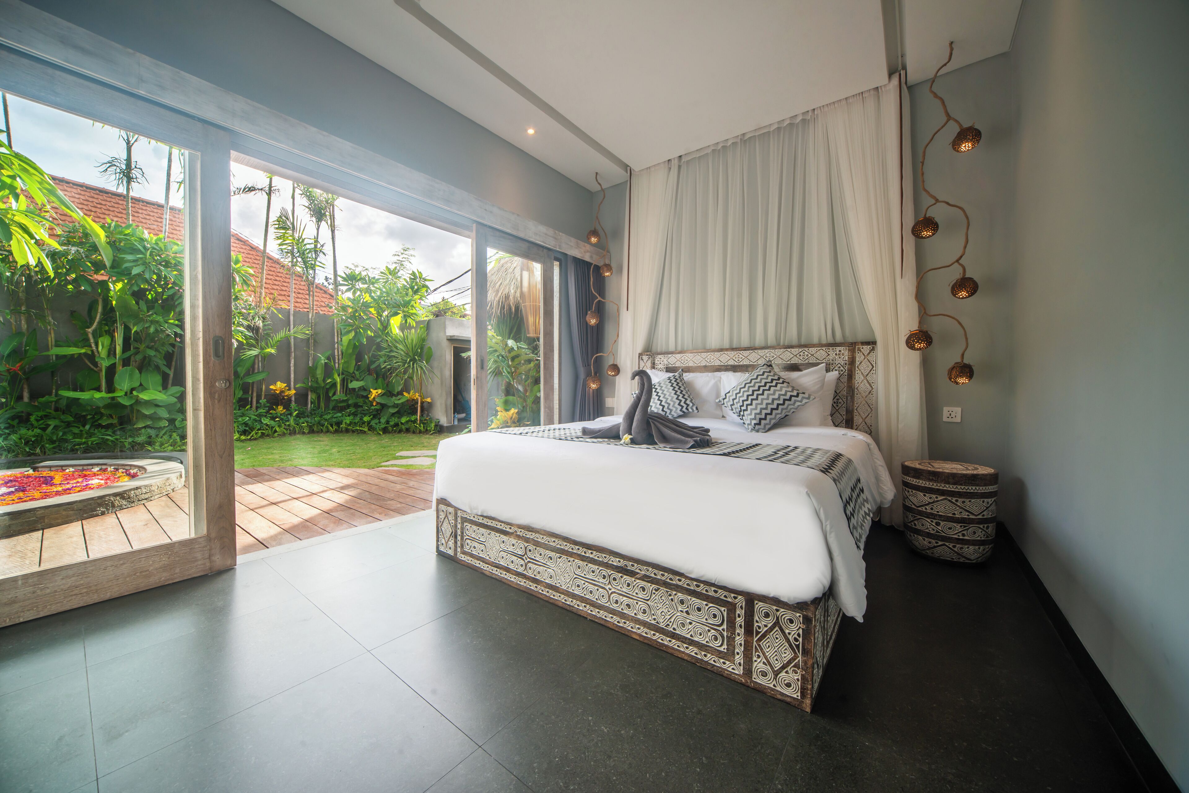 A bedroom with a large bed, a view of a garden, and a sliding glass door.