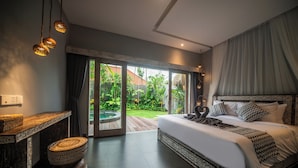 Een slaapkamer met een groot bed, een houten nachtkastje, een kleine ronde tafel en uitzicht op een tuin via een schuifdeur.