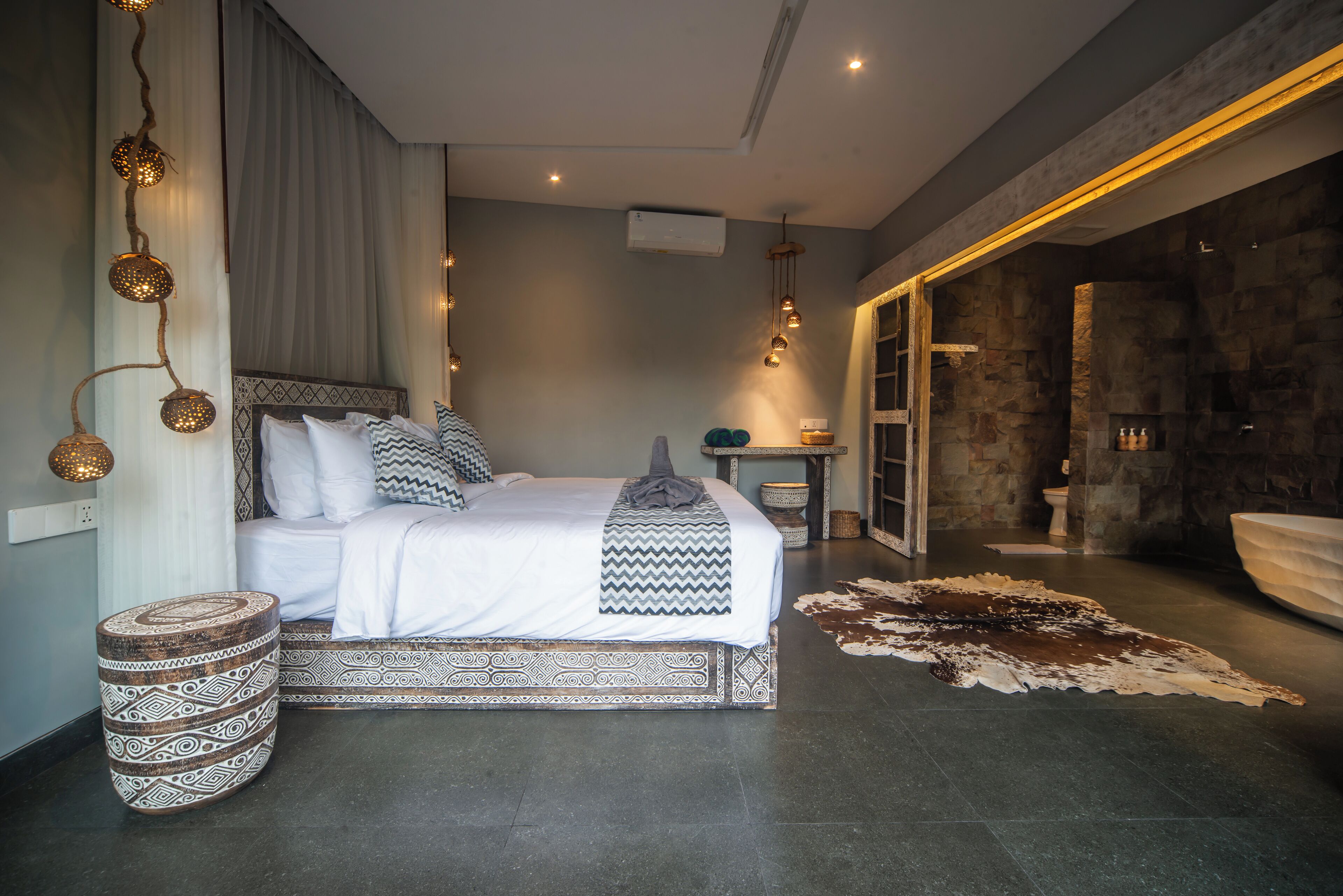 A modern bedroom with a large bed, a stone wall, and a bathroom with a bathtub.