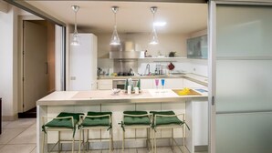 A modern kitchen with a central island, four pendant lights, and green cushioned stools. - Ludo's House (Napoli)