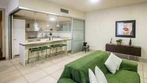 A modern living room with a green sofa, a kitchen area with a bar, and a sliding glass door leading to a balcony. - Ludo's House (Napoli)