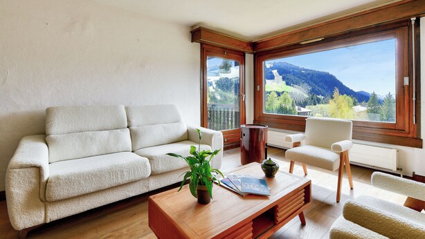 A modern living room with a sofa, armchairs, a coffee table, and a view of a mountain landscape through large windows. - Apartment Mont d'Arbois Megeve - Ski in/out (Megève)