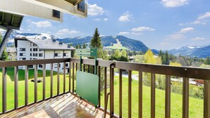 A balcony with a view of a mountain landscape, a building with a sloped roof, and a green sign. - Apartment Mont d'Arbois Megeve - Ski in/out (Megève)