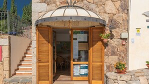 A stone building with a wooden door and a staircase leading up. - Crystal Pool Village In Tanaunella (Budoni)