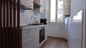 A kitchen with light wood flooring, white cabinets, a gas stove, and a window providing natural light. - 1 Bedroom Apartment - 1 Bathroom - Large Living Room - San Pietro Station (Roma)