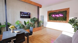 A modern interior with a wooden ceiling, a flat-screen TV, a neon sign reading "The Holy Sea", and various indoor plants. - 1 Bedroom Apartment - 1 Bathroom - Large Living Room - San Pietro Station (Roma)
