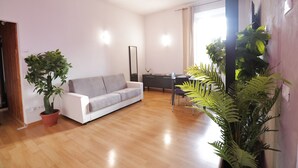 A modern living room with a white sofa, a dining table, and potted plants. - 1 Bedroom Apartment - 1 Bathroom - Large Living Room - San Pietro Station (Roma)
