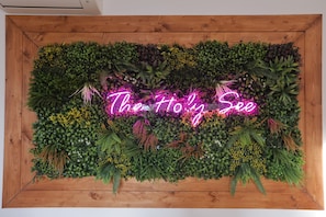 A wall decorated with various plants and a neon sign that reads "The Holy See". - 1 Bedroom Apartment - 1 Bathroom - Large Living Room - San Pietro Station (Roma)