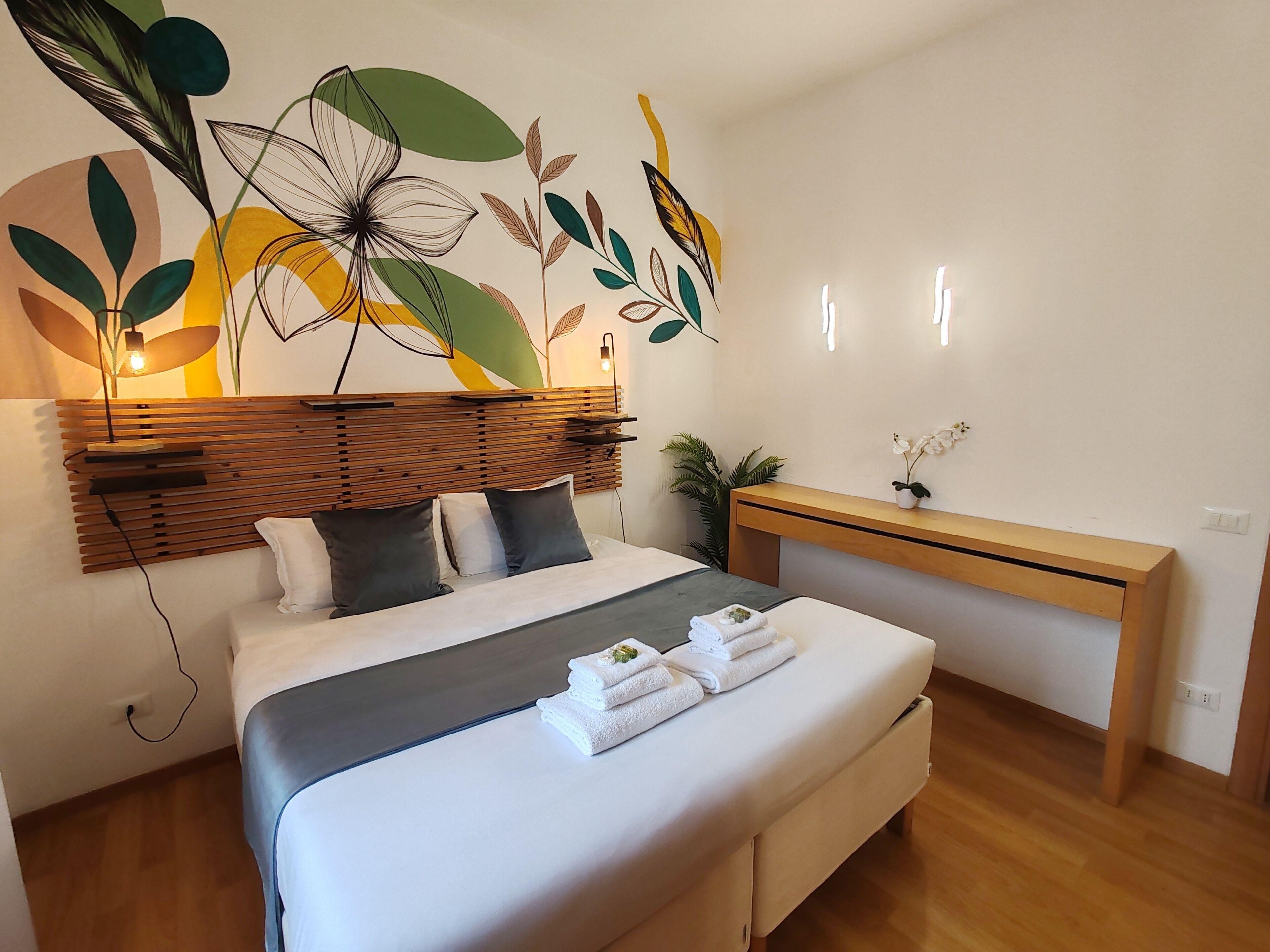 A modern bedroom with a wooden headboard, a bed with white bedding, a bedside table with a lamp, and a wall art piece.