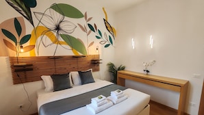 A modern bedroom with a wooden headboard, a bed with white bedding, a bedside table with a lamp, and a wall art piece. - 1 Bedroom Apartment - 1 Bathroom - Large Living Room - San Pietro Station (Roma)