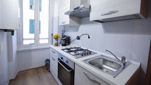A modern kitchen with white cabinets, a gas stove, a sink, and a window with blue shutters.